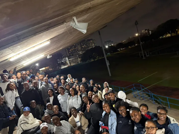 Students packed together for a night gathering under the stand, the city behind them